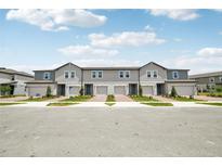 Row of townhomes with gray siding, individual garages, and well-maintained landscaping at 16466 Bird Of Paradise Ave, Clermont, FL 34714