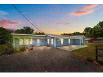 Charming single-story home with gravel driveway, blue siding, and a peaceful residential setting at dusk at 55119 5Th St, Astor, FL 32102