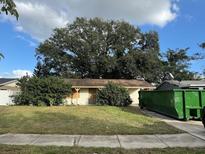 Front of the home with a large tree and a dumpster in the driveway at 2115 Messina Ave, Orlando, FL 32811