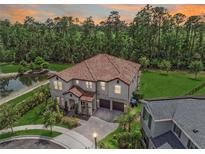 Stunning aerial view of a two-story home with a tile roof, lush landscaping, and a serene pond at 8478 Elba Isle Ct, Windermere, FL 34786