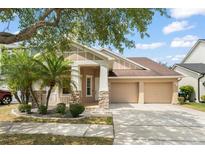 Charming home with a two-car garage, a covered porch, stone accents, manicured landscaping, and palm trees at 14537 Cheever St, Orlando, FL 32828