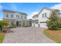 Beautiful white home featuring a brick driveway, front porch with rocking chairs, and a three-car garage at 907 Celadon St, Winter Garden, FL 34787