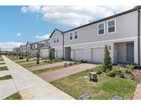Row of two-story townhomes featuring light gray siding, white trim, individual garages, and brick driveways at 16395 Bird Of Paradise Ave, Clermont, FL 34714