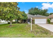Charming single-story home featuring a two-car garage and lush front lawn with mature landscaping under a sunny blue sky at 26807 Bull Run, Leesburg, FL 34748