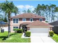 Charming two-story home featuring a well-manicured lawn, a two-car garage, and lush tropical landscaping at 140 Elgin Blvd, Davenport, FL 33897