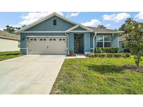 Charming blue one-story home featuring a two-car garage and well-manicured lawn on a sunny day at 6768 Coral Berry Dr, Mount Dora, FL 32757