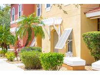 Townhome exterior featuring colorful stucco, lush landscaping, and shuttered windows with pergola at 1000 Park Club Dr, Kissimmee, FL 34746