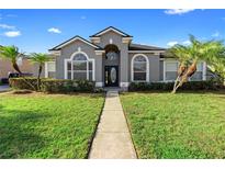 Charming gray home featuring tropical landscaping, arched windows, and a pathway leading to the front door at 9885 Montclair Circle Cir, Apopka, FL 32703