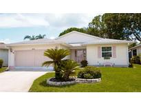 Charming single-story home with well-manicured lawn, lovely shrubbery, and a pink accent on the shutters and garage door at 32900 Crooked Oaks Ln, Leesburg, FL 34748