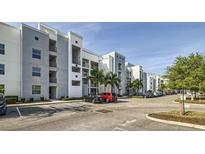 Modern condo building with ample parking, palm trees, and well-maintained landscaping under a bright sky at 4731 Clock Tower Dr # 104, Kissimmee, FL 34746