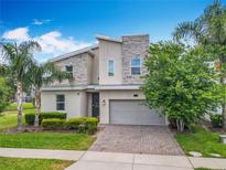 Contemporary two-story home with stone accents, paver driveway, and lush tropical landscaping at 303 Ocean Course Ave, Davenport, FL 33896