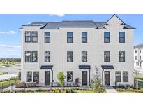 A modern three-story townhome with a white facade, black windows, and well-maintained landscaping at 6678 Juneberry Way, Winter Garden, FL 34787