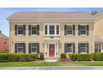 Two-story tan home with black shutters, red door, manicured landscaping, and an inviting entrance at 754 Centervale Dr, Kissimmee, FL 34747