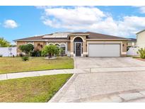 Inviting single-story home featuring a manicured lawn, charming landscaping, solar panels, and a brick-paved driveway at 5113 Sage Way, Kissimmee, FL 34758
