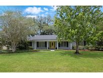 Charming single-story home featuring a manicured lawn, mature trees, and a welcoming yellow front door at 1204 Howell Creek Dr, Winter Springs, FL 32708