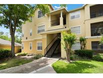 Inviting yellow condo building featuring well-kept landscaping, a stairway, and balcony, all set against a blue sky and green trees at 2652 Robert Trend Jones # 2652, Orlando, FL 32835