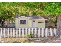 Charming yellow cottage-style home with a white picket fence and lush green trees at 5750 Delta St, Orlando, FL 32807