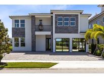 Modern two-story home featuring a stone facade, balcony with hanging chair, and a glass paneled two-car garage at 300 Muirfield Loop, Reunion, FL 34747