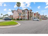 View of the condo community, showing the multi-colored facade and palm trees and ample parking on a sunny day at 2213 Grand Cayman Ct # 1138, Kissimmee, FL 34741