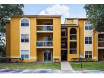 A yellow two story condo building with stairwells and lush trees on a bright day at 5267 Images Cir # 102, Kissimmee, FL 34746