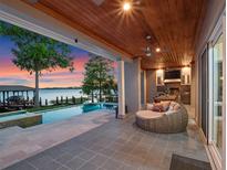 Covered patio boasts an outdoor kitchen and cozy seating area next to a sparkling pool and serene lake view at 9916 Lone Tree Ln, Orlando, FL 32836