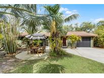 Charming single-story home featuring a lush, tropical landscaped yard and patio area with stylish umbrella at 1200 Auger Dr, New Smyrna Beach, FL 32168
