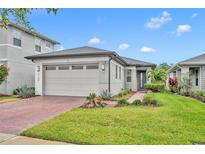 Charming single-Gathering home featuring a well-manicured lawn, gray paint, brick driveway, and two-car garage at 3149 Songbird Cir, Harmony, FL 34773