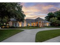 Stunning exterior of home with stone entryway, lush landscaping and circular driveway at sunset at 5025 Down Point Ln, Windermere, FL 34786