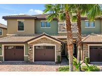 Townhouse with stone accents, a brown garage door, brick driveway and some palm trees at 8990 Azalea Sands Ln # 8990, Davenport, FL 33896