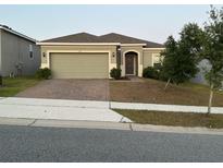 Charming single-story home featuring a two-car garage, brick driveway, and manicured landscaping at 176 Jensen Dr, Groveland, FL 34736