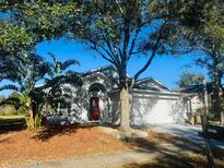 Charming single-story home with a well-maintained front yard and mature trees, featuring a red front door and attached garage at 17517 Silver Creek Ct, Clermont, FL 34714