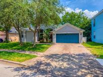 Charming single-story home with well-manicured lawn, brick driveway, mature trees, and a vibrant blue two-car garage door at 6542 Lake Pembroke Pl, Orlando, FL 32829