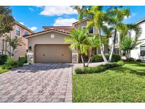 Charming two-story home featuring a lush lawn, mature palm trees, brick paver driveway, and an attached two-car garage at 8150 Prestbury Dr, Orlando, FL 32832