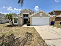 Tan single-story home featuring a 2-car garage, palm trees, and beautiful landscaping at 3049 Buckeye Pointe Dr, Winter Haven, FL 33881