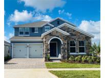 Two-story home with stone accents, a paved driveway, manicured lawn and a two car garage under a blue sky at 15378 Gilligan Ct, Winter Garden, FL 34787
