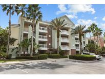 Inviting condo building with multiple balconies, palm trees, lush landscaping, and ample parking for residents and guests at 7660 Whisper Way # 402, Reunion, FL 34747