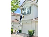Exterior view of home's facade, featuring a tile roof, two-car garage, and landscapers on ladders doing exterior work at 7054 Cadiz Blvd, Orlando, FL 32819