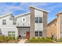 Modern two-story home featuring a stone facade, gray siding, and a vibrant red front door at 4375 Scene Ln, Kissimmee, FL 34746