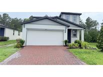 Two-story home with a white two car garage, gray roof, and a brick paver driveway at 877 Rivers Crossings St, Clermont, FL 34714