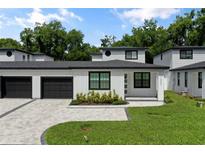 Modern townhome with white siding, black trim, an attached garage, a landscaped yard, and a paver driveway at 1002 Farmstead St, Eustis, FL 32736