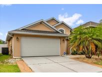 Beige single Gathering home with a concrete driveway leading to a two car garage and tropical landscaping at 14617 Keelford Way, Orlando, FL 32824