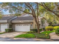 Charming townhome featuring a gray exterior, tile roof, and a two-car garage, complemented by lush landscaping and a tree canopy at 3987 Lancashire Ln # 3987, Longwood, FL 32779