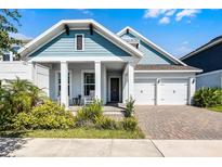 Charming two-story home with blue accents, a welcoming front porch, and a brick driveway leading to a two-car garage at 14925 Lebeau Loop, Winter Garden, FL 34787