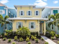 Charming two-story yellow beach home with light blue shutters, landscaped yard, and walkway to the front door at 3036 Parrot Head Pl, Kissimmee, FL 34747
