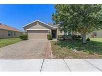 Charming home featuring a two-car garage, brick paver driveway, and mature landscaping at 10138 Lenox St, Clermont, FL 34711