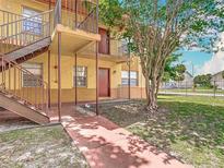 View of the exterior of the yellow and brown apartment building showing the yard, entryway, and staircase at 744 Wyman Ct # 744, Orlando, FL 32809