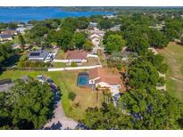 Aerial view of a home with a screened-in pool, manicured lawn and mature trees near a lake at 10545 Parkway Dr, Clermont, FL 34711