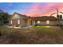 Charming single-story brick home featuring a well-maintained lawn and mature trees under a beautiful sunset sky at 10545 Parkway Dr, Clermont, FL 34711