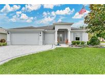 Inviting single-story home featuring a well-manicured lawn, three-car garage, and a charming American flag at 4002 Richmond Xing, Leesburg, FL 34748