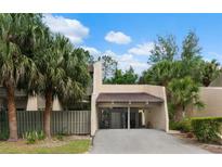 Beige two-story condo with car port, palm trees and garden against a blue and cloudy sky at 115 Tomoka Trl # 115, Longwood, FL 32779